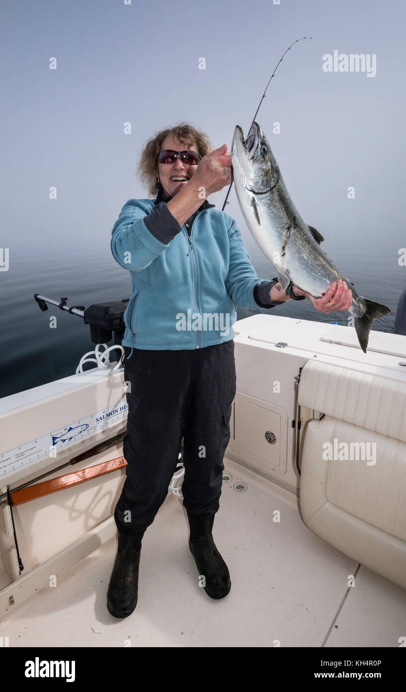 Donna di mezza età in barca da pesca con catturato il salmone, mattinata nebbiosa a Johnstone Strait fuori dall'Isola di Vancouver, British Columbia, Canada Foto Stock
