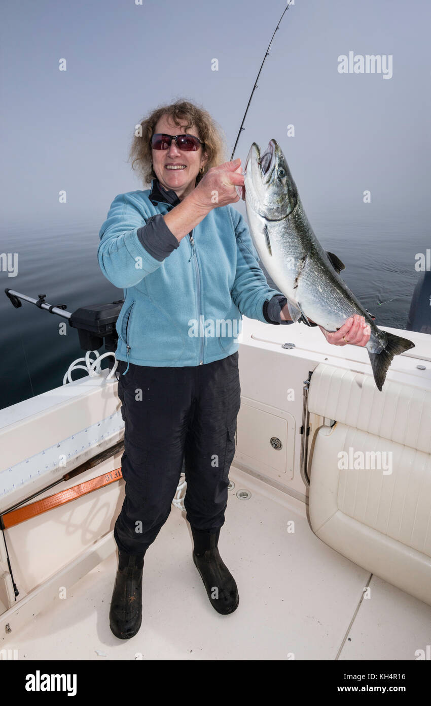 Donna di mezza età in barca da pesca con catturato il salmone, mattinata nebbiosa a Johnstone Strait fuori dall'Isola di Vancouver, British Columbia, Canada Foto Stock