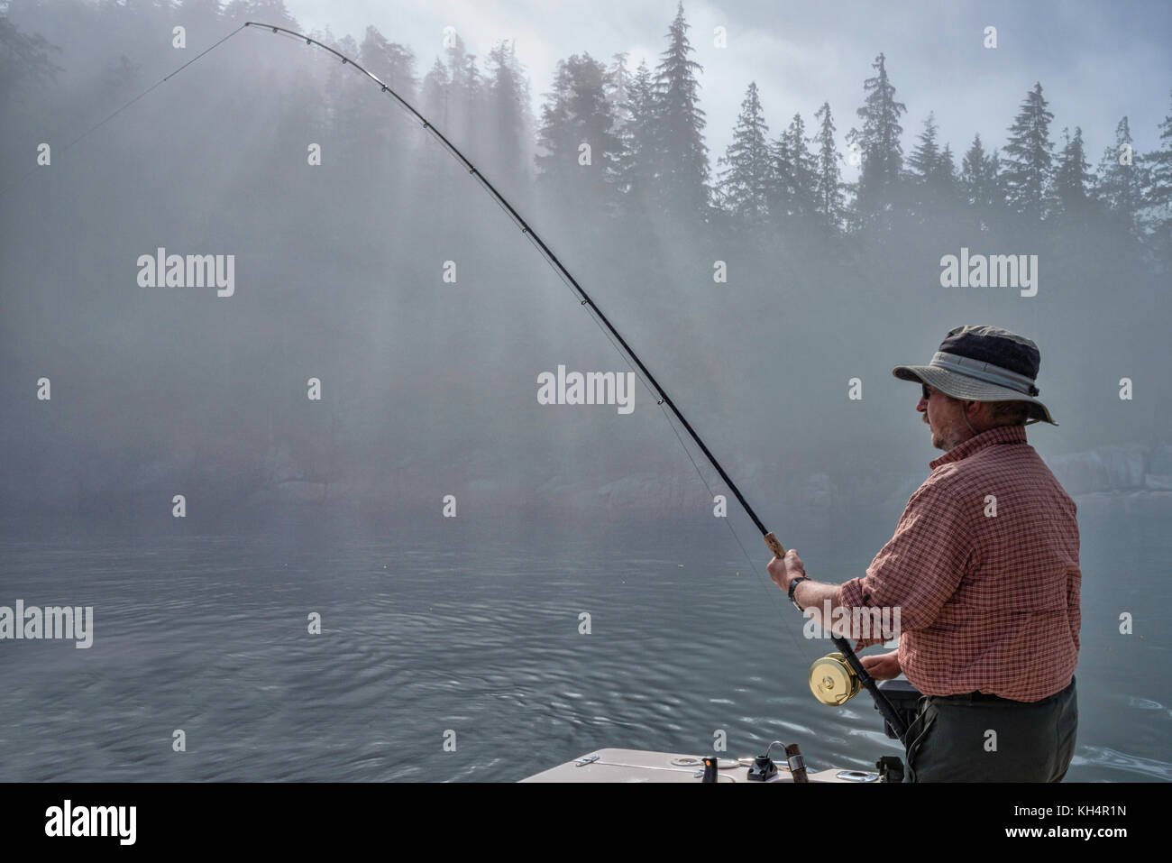 L'uomo con la canna da pesca, sulla barca da pesca, mattinata nebbiosa a Johnstone Strait fuori dall'Isola di Vancouver, British Columbia, Canada Foto Stock