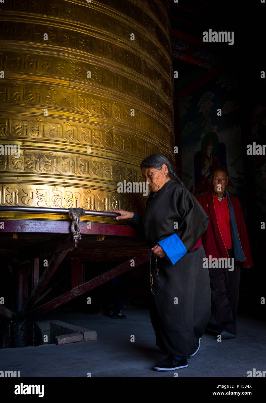 Pellegrini tibetani girando enorme ruota di preghiera nel monastero di Rongwo, Tongren County, Longwu, Cina Foto Stock