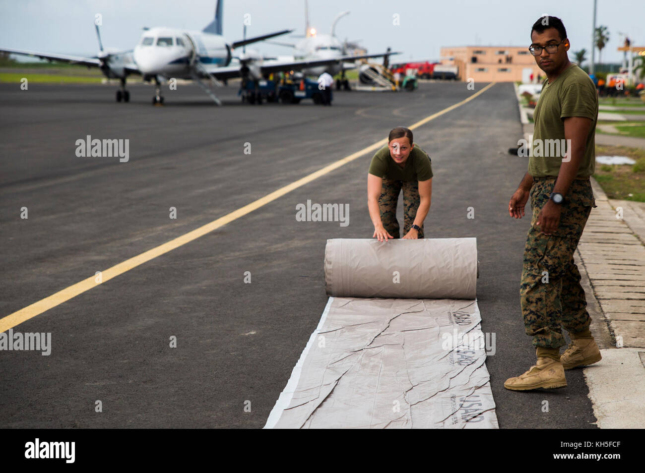 Stati Uniti Marines con Joint Task Force - Isole Sottovento srotolare un U.S. Agenzia per lo Sviluppo Internazionale tarp per preparare materiali di consumo per la distribuzione a Douglas-Charles Aeroporto di Melville Hall, Dominica, Settembre 29, 2017. A richiesta di USAID, JTF-li ha distribuito degli aerei e i membri del servizio per contribuire a fornire aiuti umanitari alla Dominica dopo il passaggio dell uragano Maria. La task force è un militare statunitense di unità composta di Marines, soldati, marinai e aviatori, e rappresenta U.S. Comando Sud la risposta primaria per gli uragani che hanno colpito i caraibi orientali. (U.S. Foto Stock