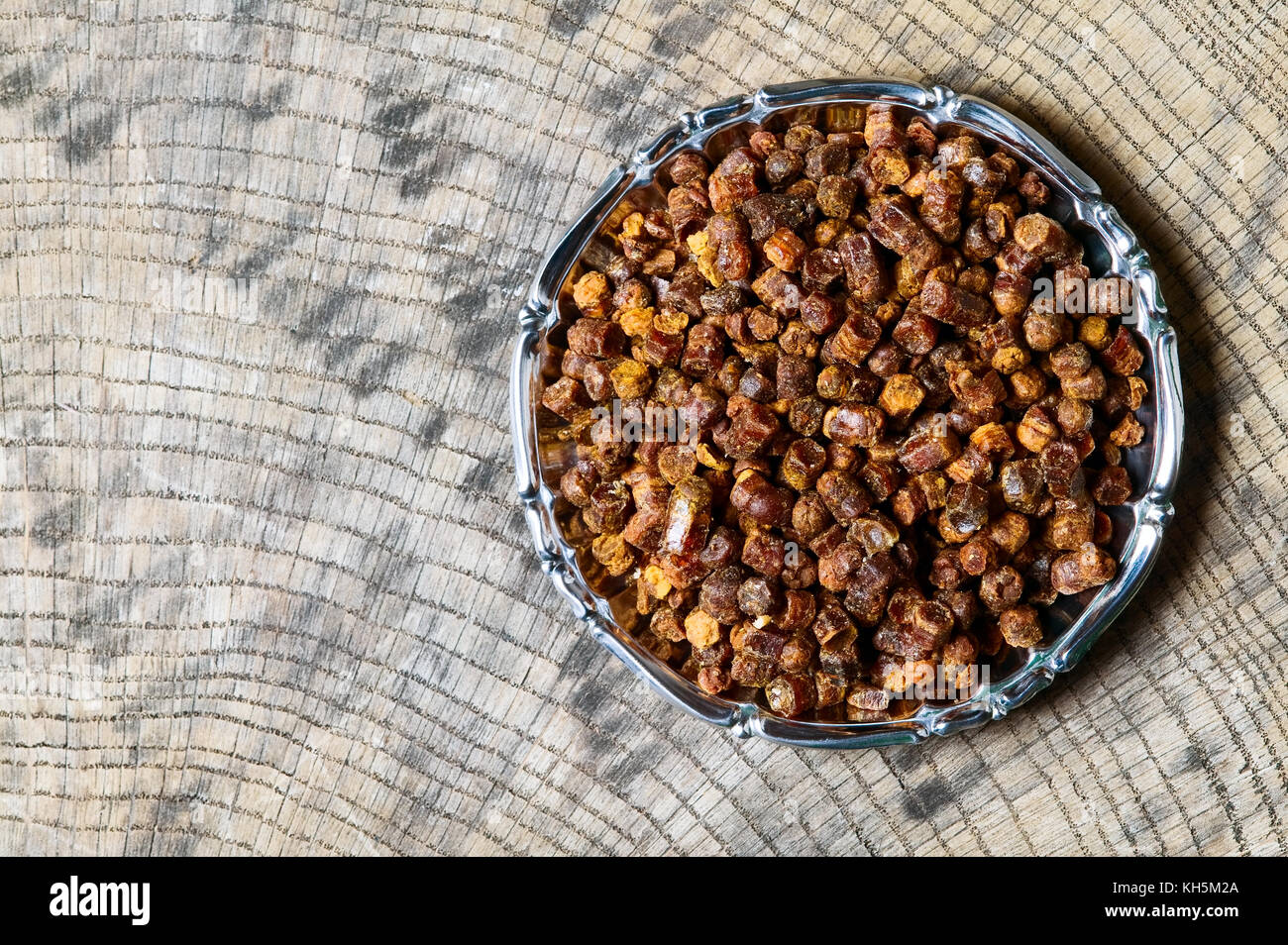 Granuli di propoli all'interno della piastra su sfondo di legno, prodotti apistici Foto Stock