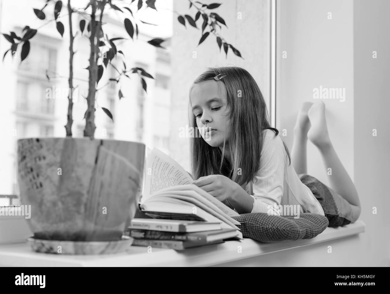 La ragazza è sdraiato sul davanzale della finestra e la lettura di un libro bianco e nero. Foto Stock