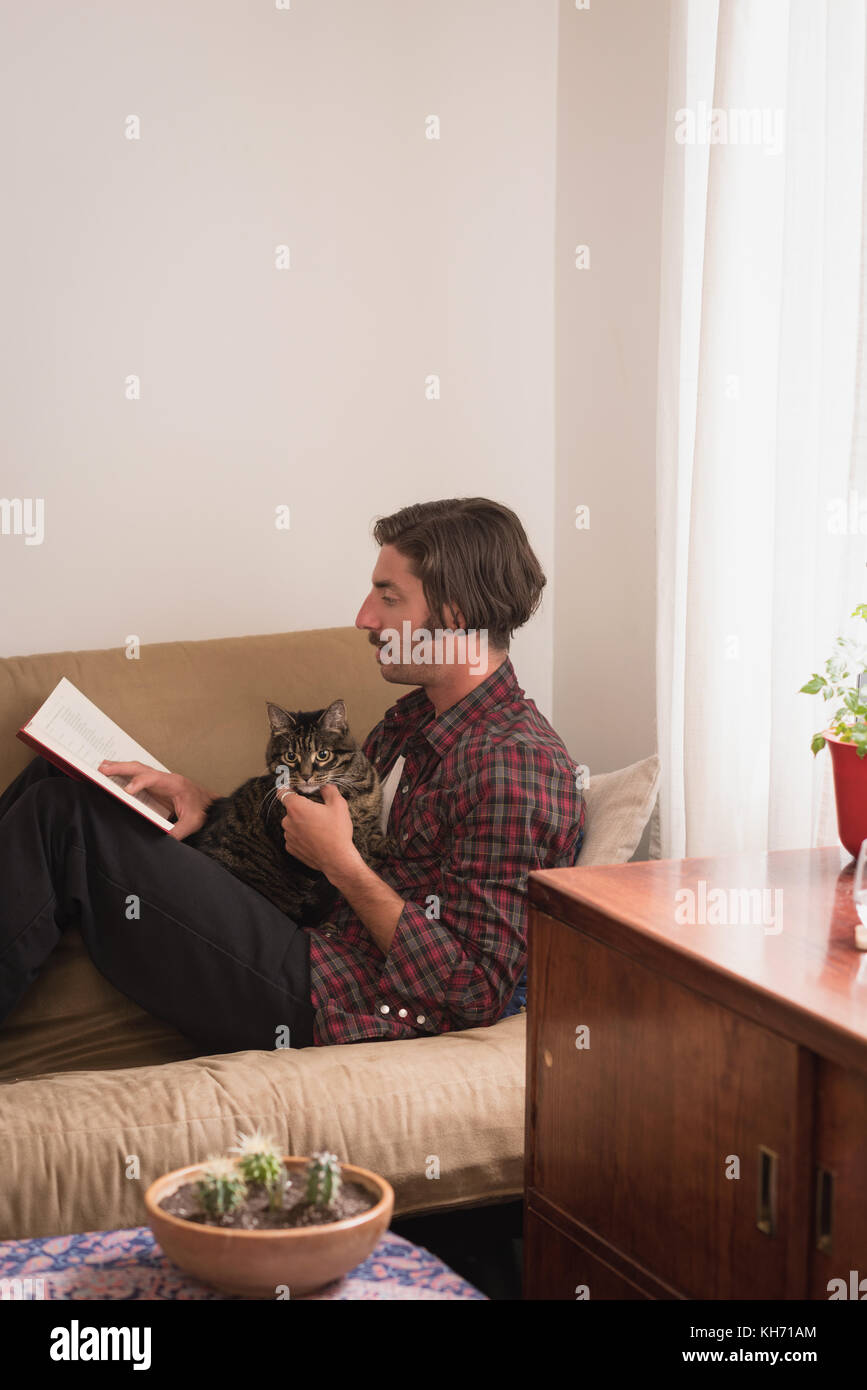 L'uomo con il suo gatto per leggere un romanzo sul divano di casa Foto Stock