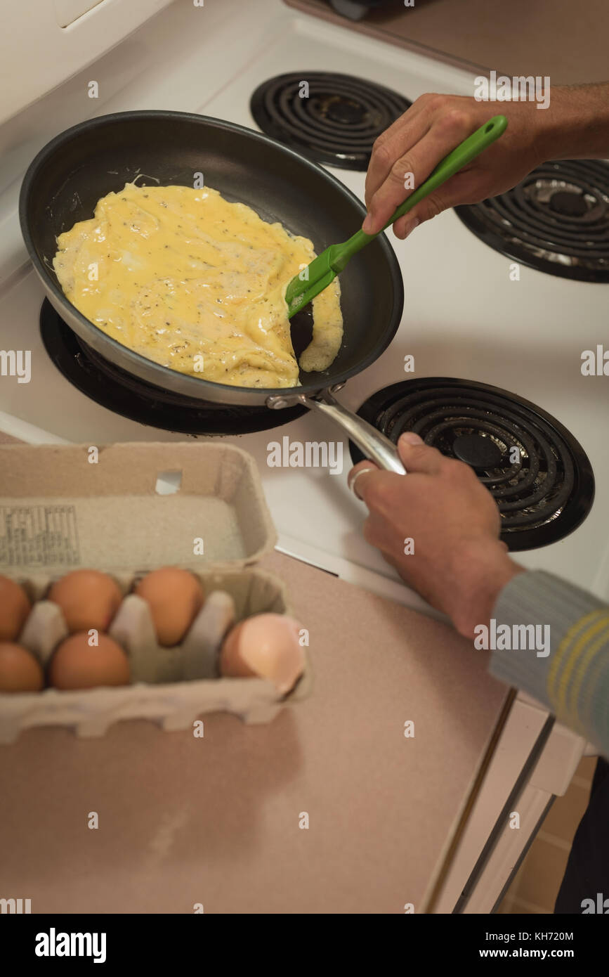 L'uomo la preparazione di uova strapazzate in padella in cucina Foto Stock