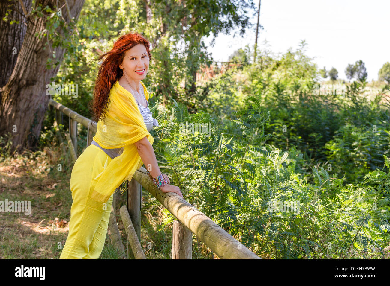 Elegante donna brasiliana con mantello giallo e scialle e silver top è sorridente in un parco verde Foto Stock