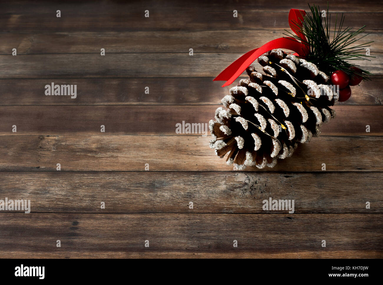 Giant pigna decorata con glitter, rosso holly bacche, fir, nastro e mini led luci su legno marrone scuro dello sfondo con un sacco di copiare il ritmo. Foto Stock