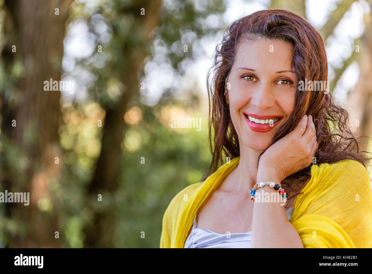 Elegante South American donna con mantello giallo e scialle e silver top è sorridente in un parco verde Foto Stock