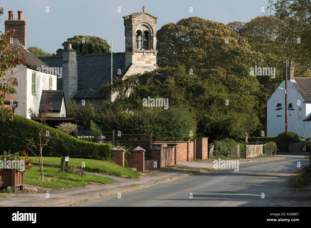 Vista lungo la tranquilla, paese rurale lane verso l'alto campanile della St Giles Church & attraente village cottages - Burnby, East Yorkshire, Inghilterra, Regno Unito. Foto Stock