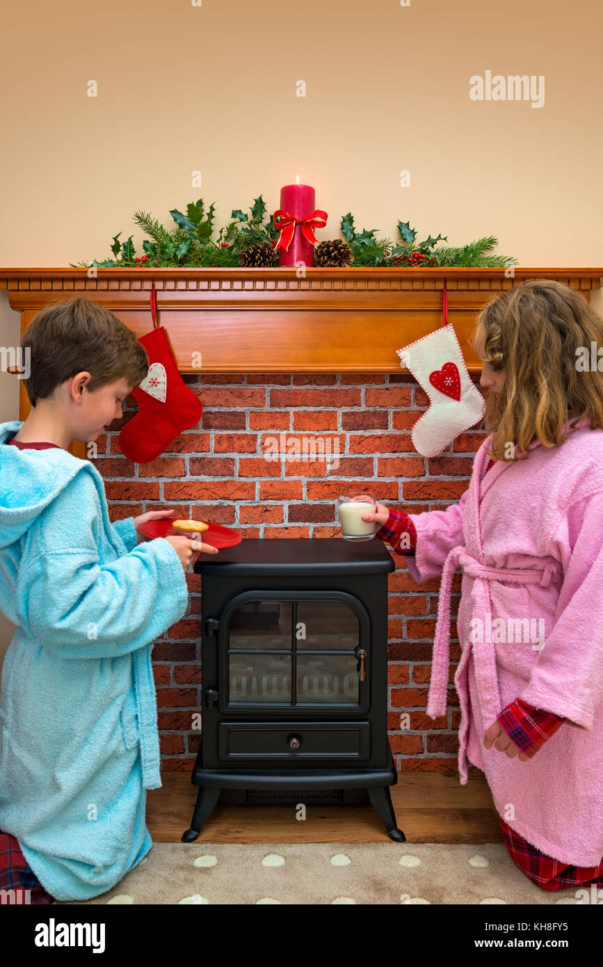Due bambini, un ragazzo e una ragazza, mettendo un bicchiere di latte e carne macinata pie / cookie per santa alla vigilia di Natale. Foto Stock