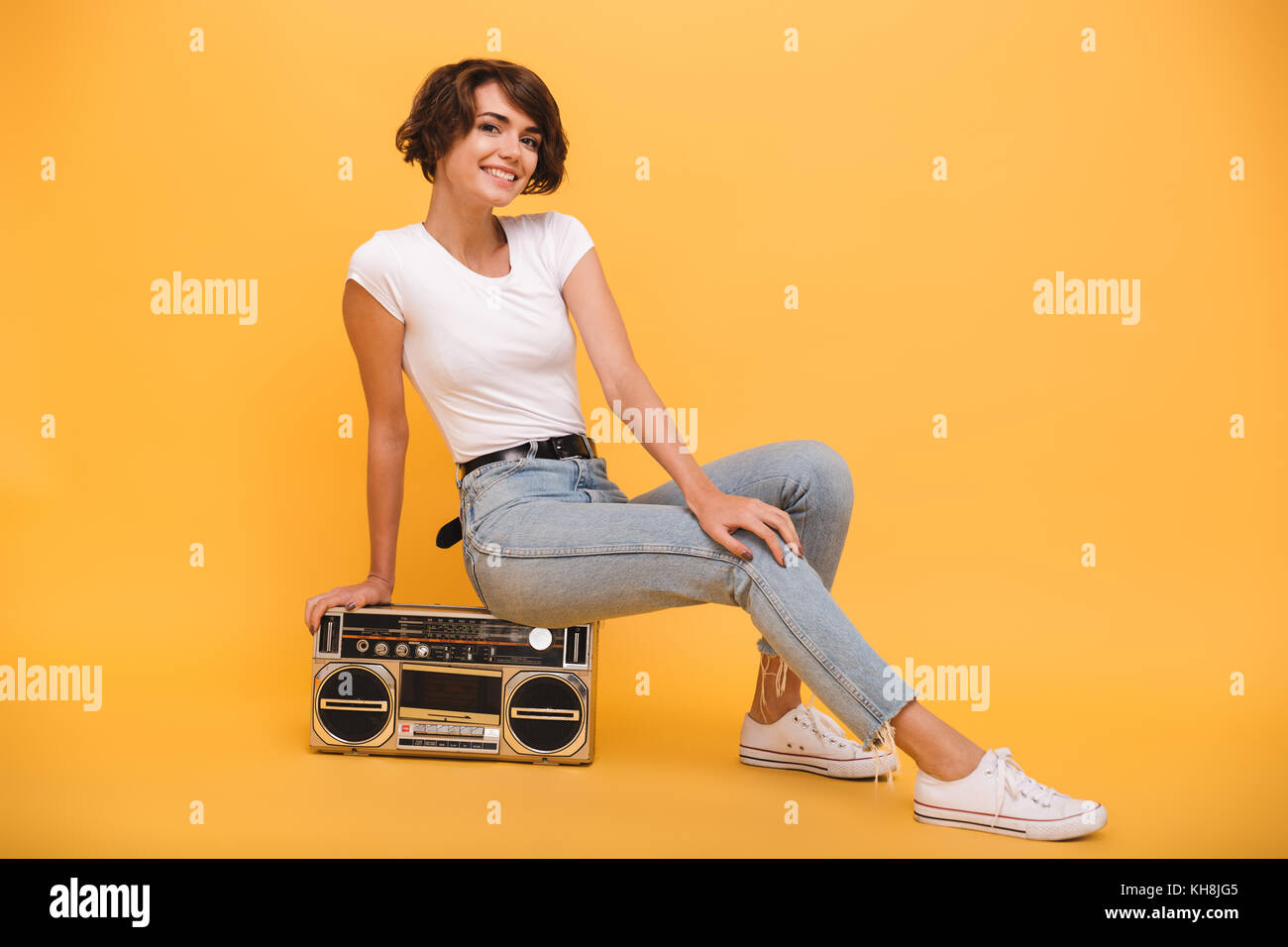 Ritratto di una gioiosa giovane ragazza seduta record giocatore e guardando la telecamera isolate su sfondo giallo Foto Stock