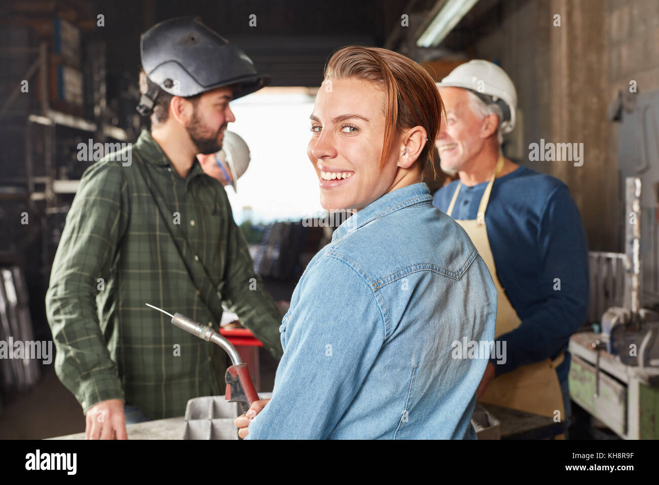 Giovane donna come lavoratore apprendista sorridente con gioia nel laboratorio di metallurgia Foto Stock