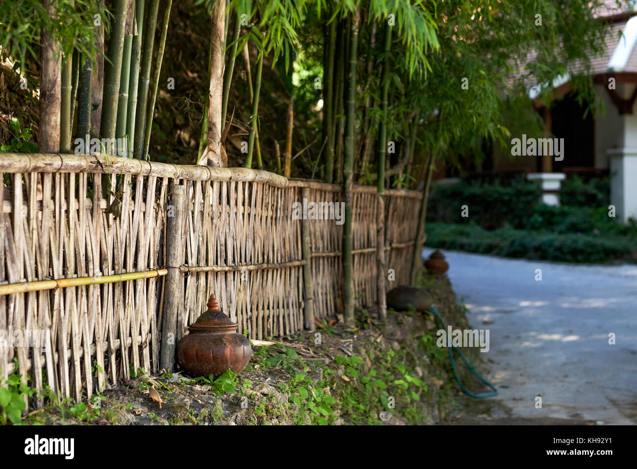 Una piccola strada di un villaggio Thai. Recinto di bambù e sfocata casa sullo sfondo. Atmosfera tranquilla per il resto Foto Stock