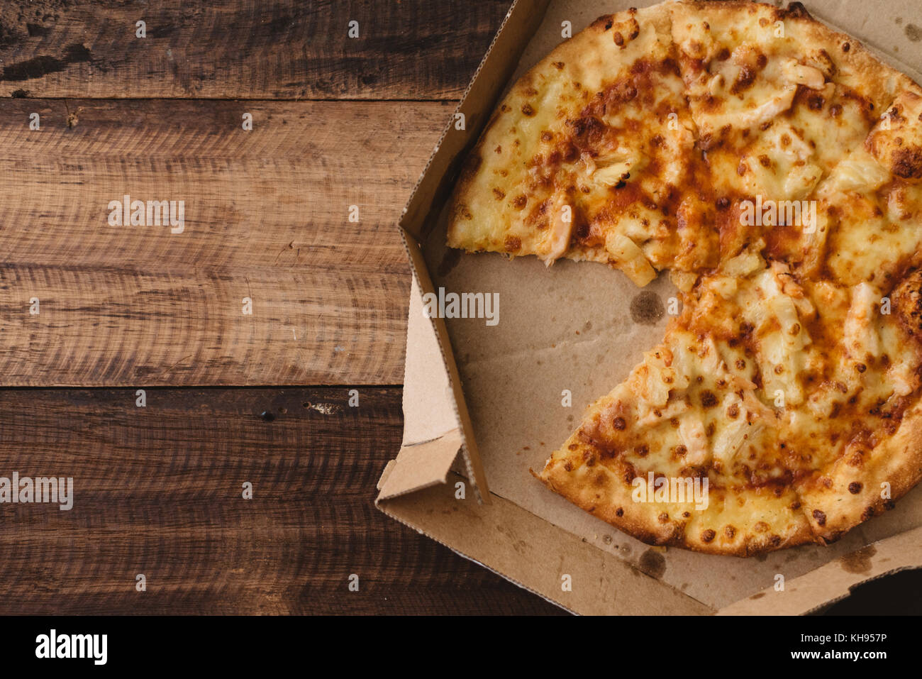La pizza con il formaggio, l'ananas e il pollo in una scatola di consegna su di un tavolo di legno Foto Stock