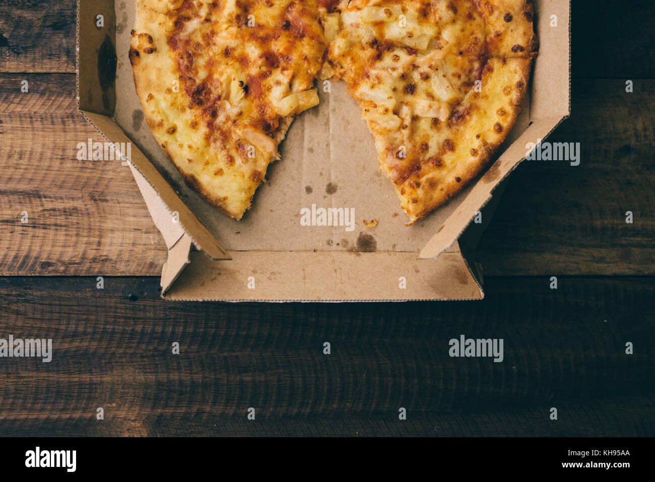 La pizza con il formaggio, l'ananas e il pollo in una scatola di consegna su di un tavolo di legno Foto Stock
