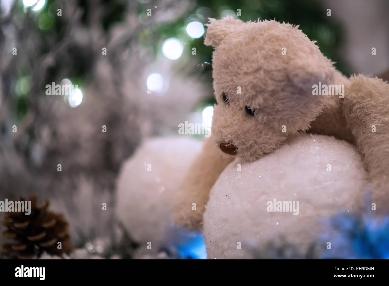 Il beige Teddy bear hugs snowballs con albero di natale e le luci sfocate in background. Foto Stock