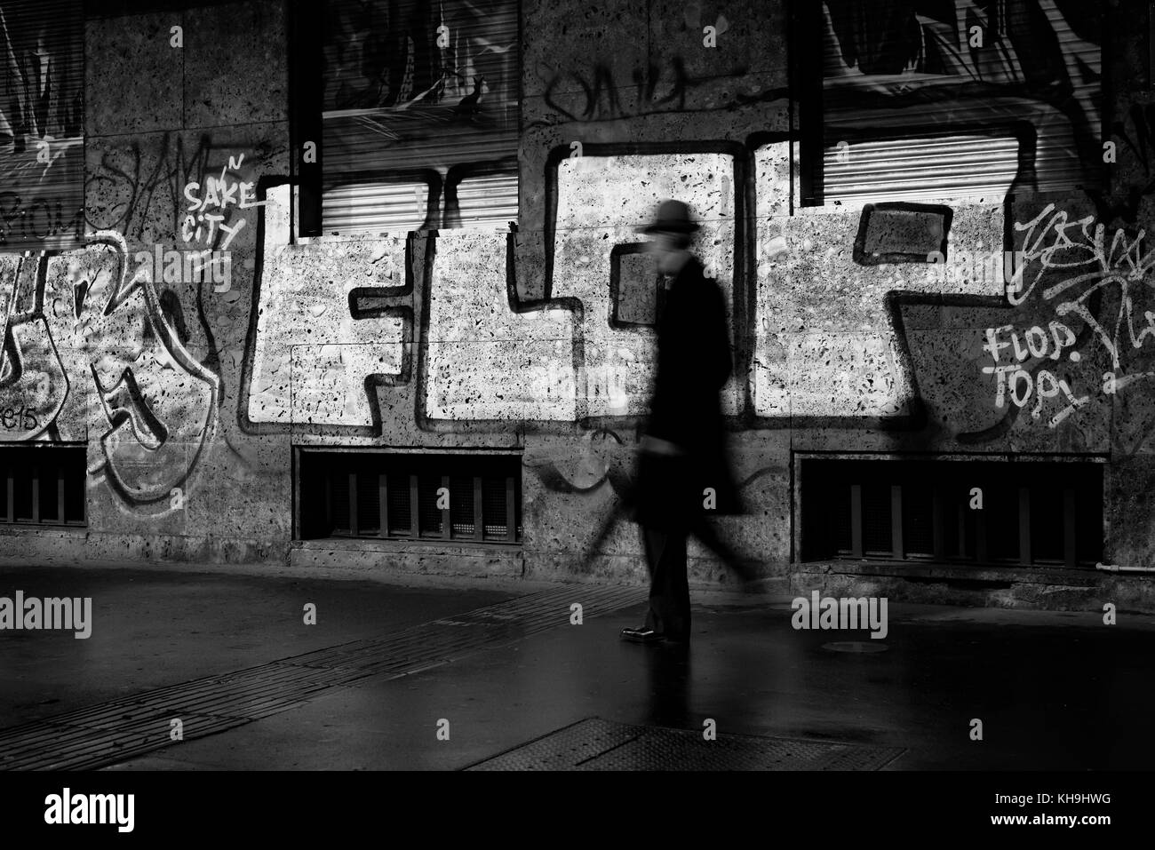 Uomo in abito borghese a piedi vicino a un murale flop di notte Foto Stock