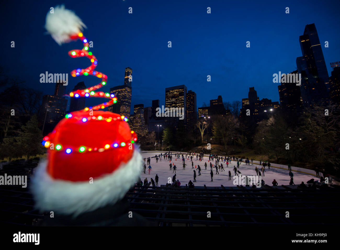 Le colorate luci di vacanza scintillanti illuminano un cappello di Babbo Natale di fronte a uno scintillante skyline della città e a una pista di pattinaggio su ghiaccio Foto Stock