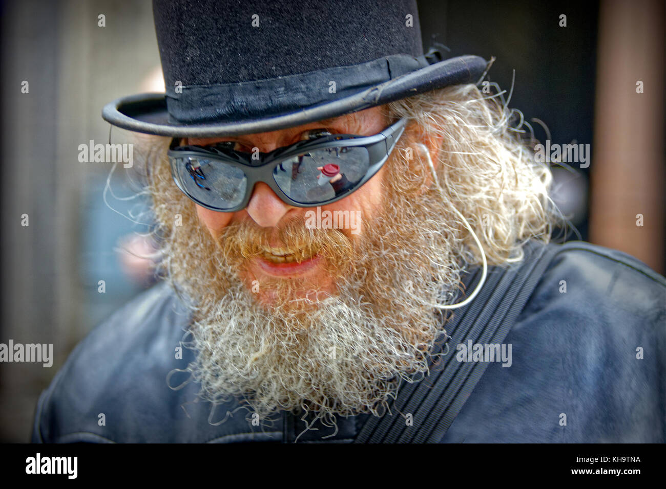 Artista locale frankie patrick robertson carattere sulla strada Bowler cappello trench coat occhiali da sole barbuto uomo felice cablato per l'audio Foto Stock
