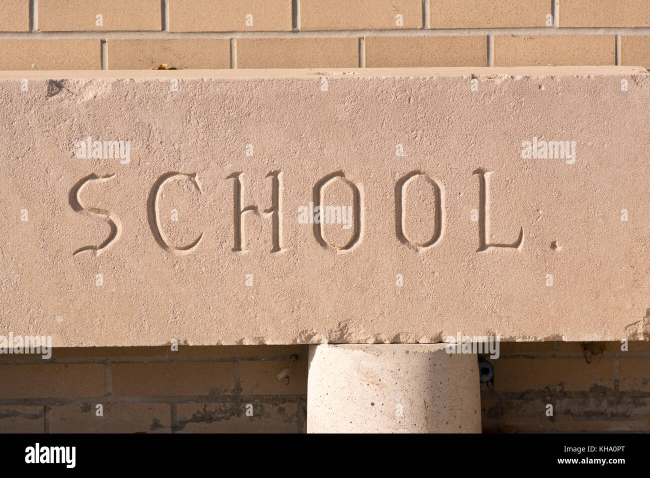 La scuola di parola incisi nella pietra con un muro di mattoni. Foto Stock