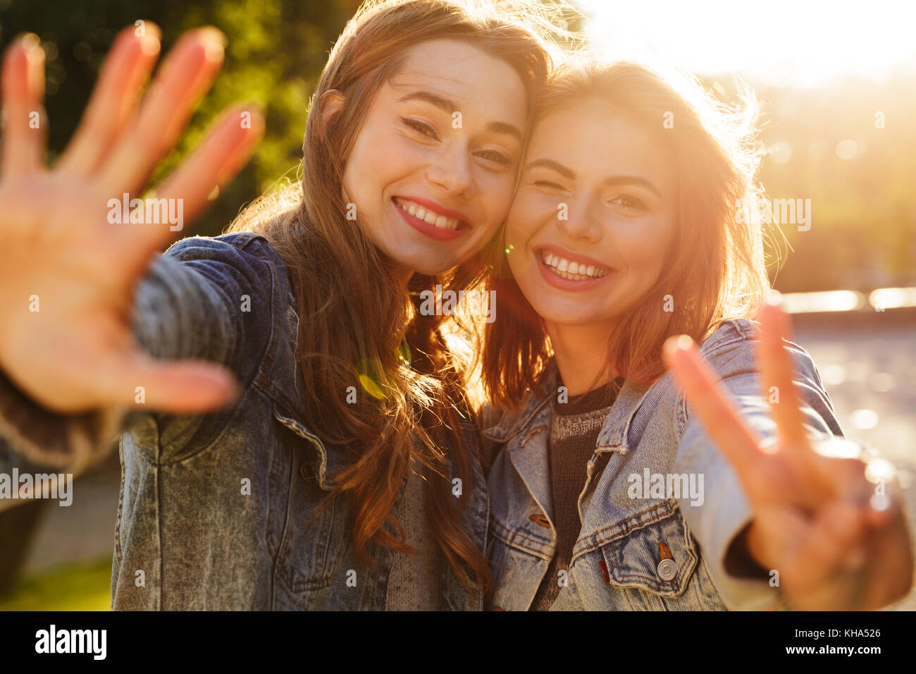 Ritratto di due sorridenti ragazze giovani sventolando la fotocamera mentre in piedi all'aperto Foto Stock