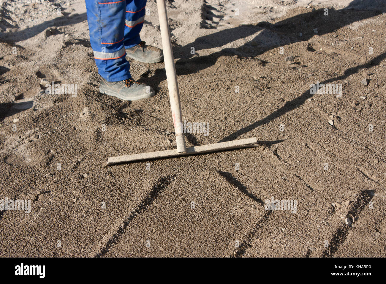 Sito in costruzione: pavimentazioni stradali preparazione, due lavoratori appiattimento della base di sabbia Foto Stock