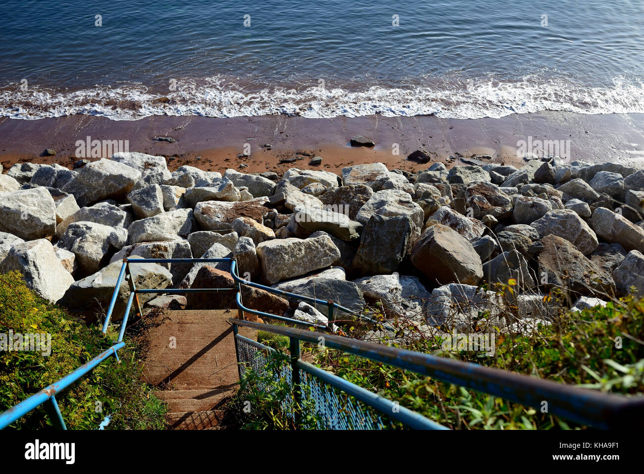 Rock armour - grandi massi accatastati contro rosso scogliere di arenaria per evitare ulteriori fenomeni di erosione da parte del mare. Foto Stock