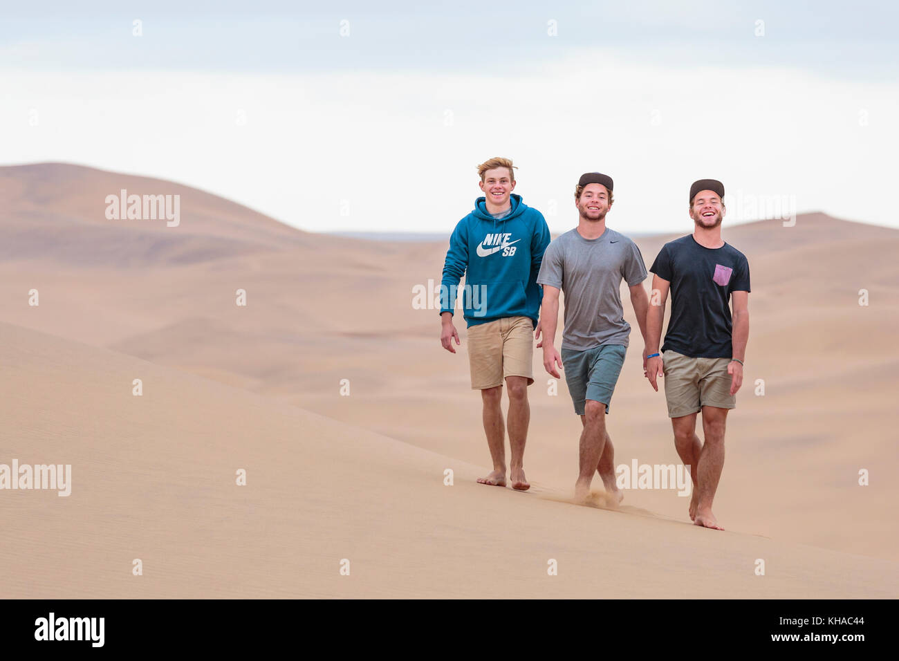 Tre giovani uomini correre sulla duna di sabbia, Namib Desert, Namibia Foto Stock