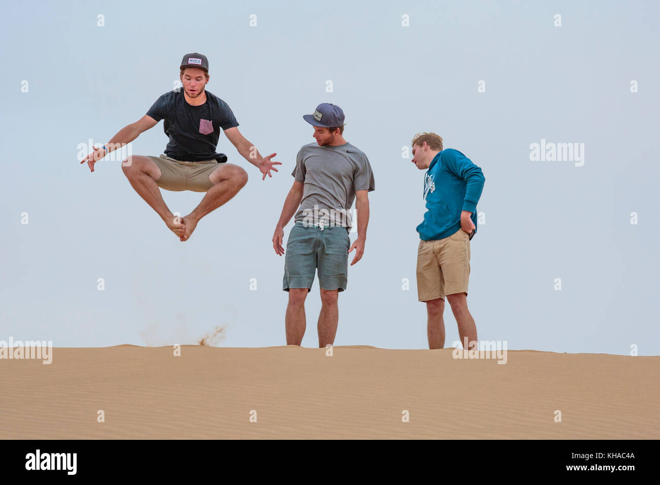 Giovane uomo salta sulla duna di sabbia, due stanno a guardare, Namibia Foto Stock