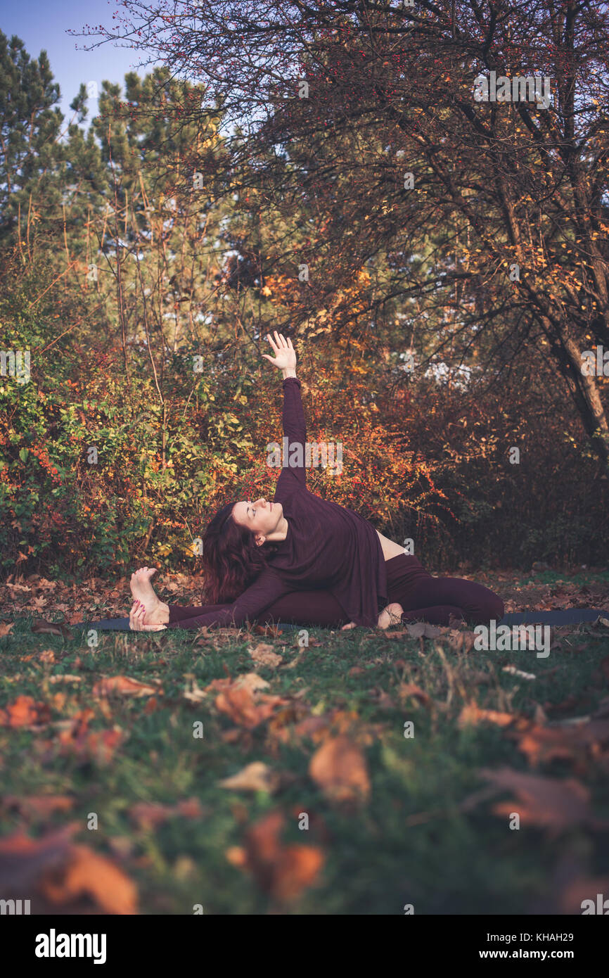 Ragazza di una luminosa giornata autunnale a praticare yoga all'aperto, facendo parivrtta janu sirsasana (giravano testa a ginocchio) pongono un lato dritto fino al di sopra Foto Stock