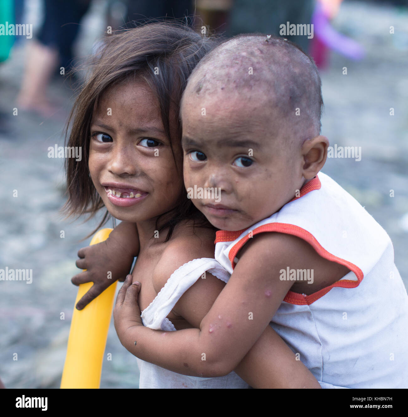 Ragazza povera con sorriso emotivo cercando di essere coraggiosi anche se avversario. avendo cura di suo fratello più piccolo. La vita nella baraccopoli di filippino. Foto Stock