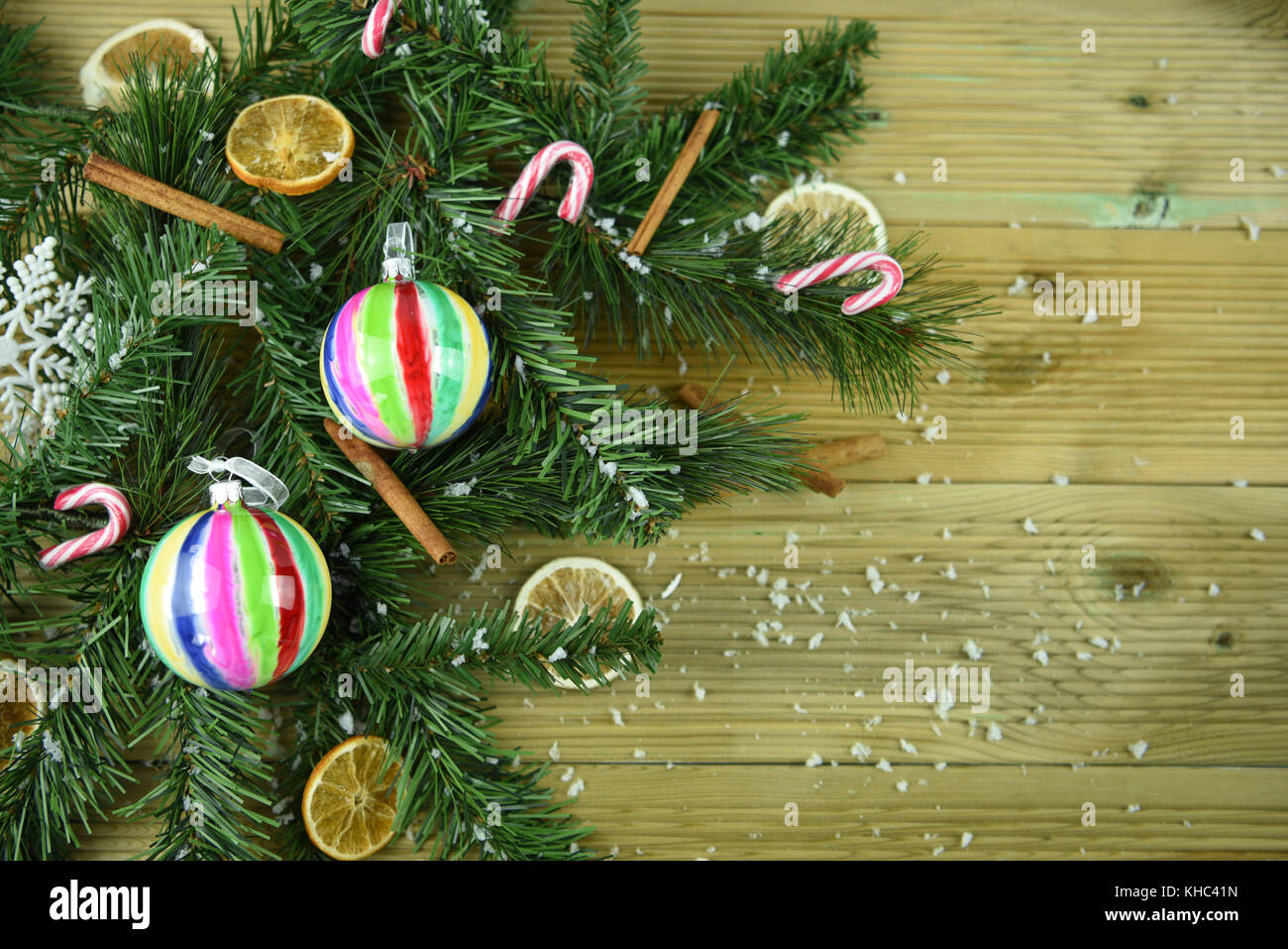 Natale immagine a colori del verde rami di albero su sfondo di legno con bastoncini di cannella arancio fette di frutta bianca e fiocchi di neve tutto spolverato di neve Foto Stock