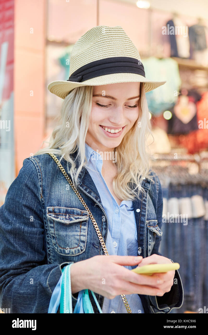 Giovane donna con cappello di paglia mentre lo shopping gode di un messaggio di testo Foto Stock