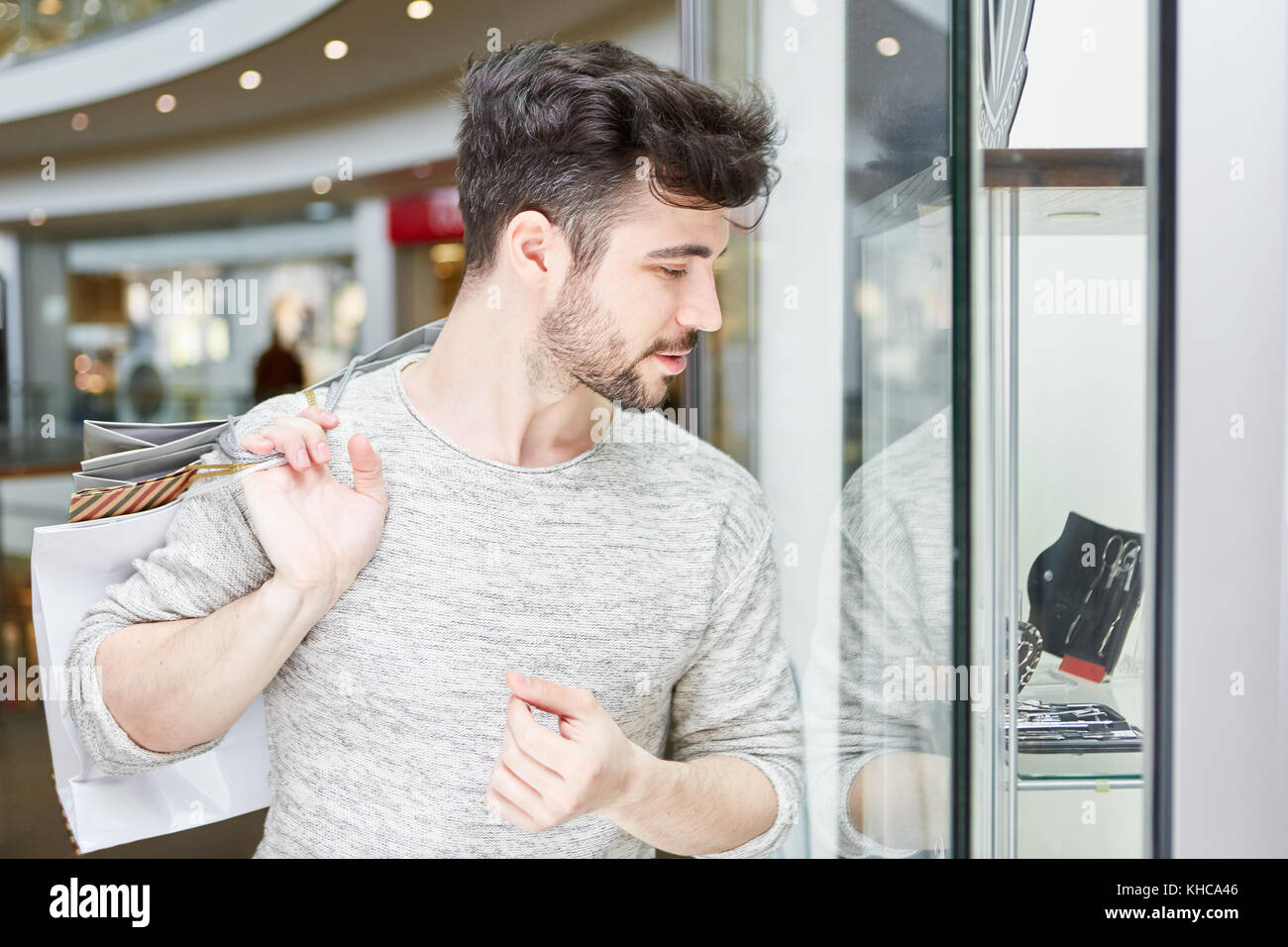 Giovane uomo con i sacchetti di shopping mentre guardando nella vetrina di un negozio. Foto Stock