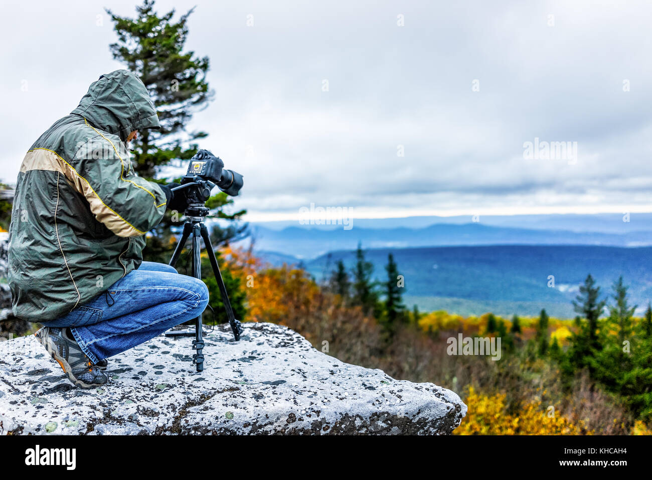 In piedi giovane fotografo con fotocamera, ingranaggio e treppiede in autunno freddo mattino nella camicia in orso rocce, West Virginia a scattare foto di sunrise Foto Stock