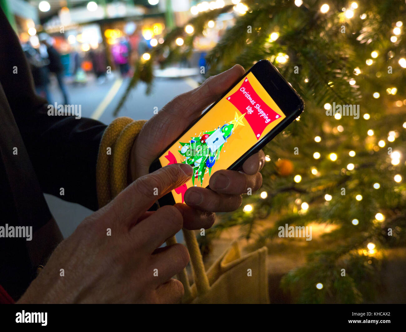 Uomo con smartphone iphone 7plus con secure bloccato lo shopping natalizio app sullo schermo, in festa albero di Natale illuminato ambiente commerciale Borough Market southwark LONDON REGNO UNITO Foto Stock
