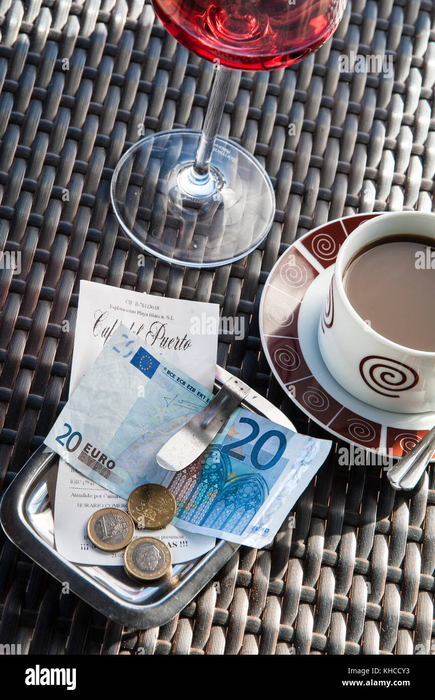 Alfresco Ristorante spagnolo tabella con Euro bill il pagamento in contanti, tazza di caffè e un bicchiere di vino rosé nell'albero di luce del sole Spagna Foto Stock