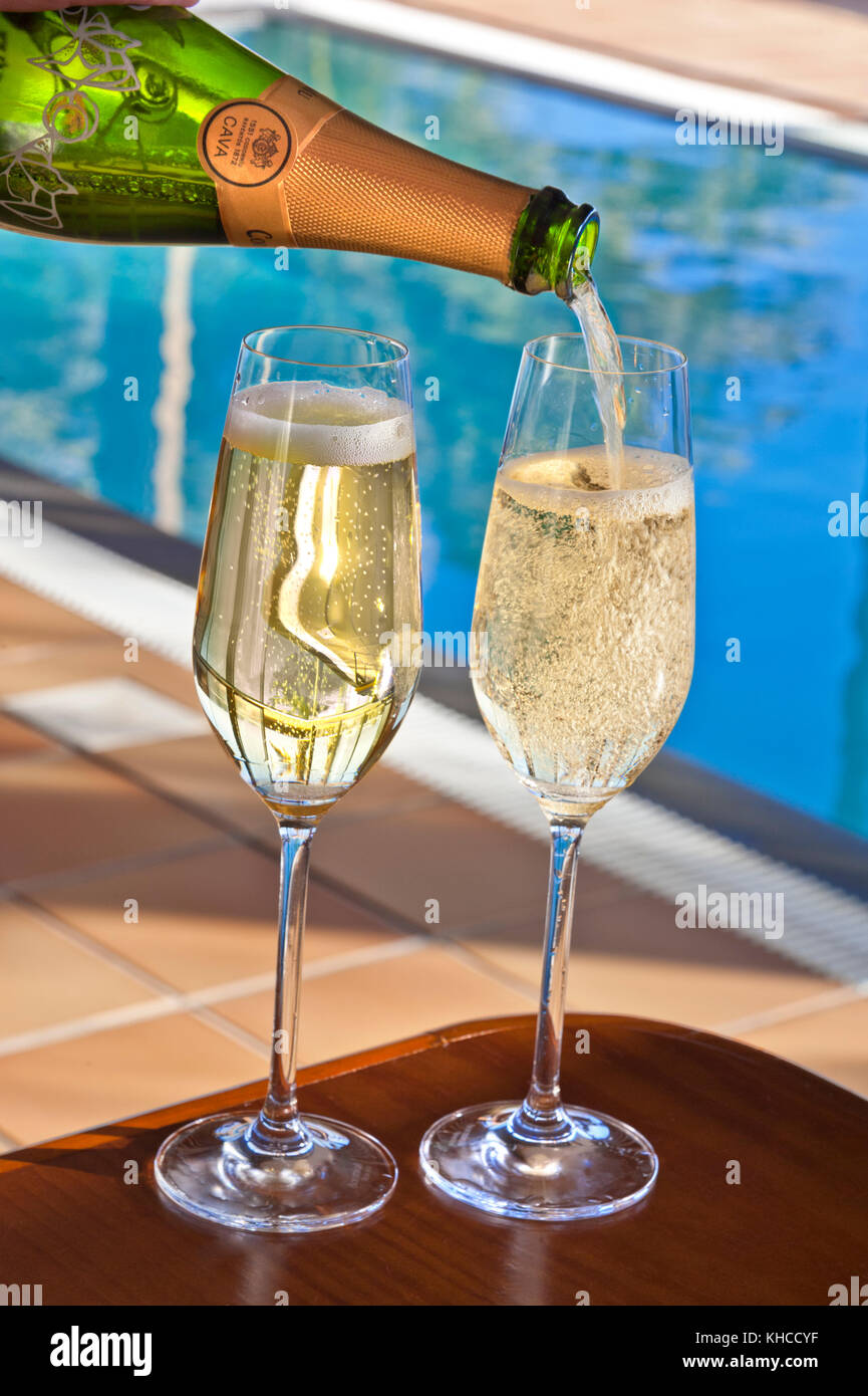 Bottiglia di spumante cava in Spagna piscina di lusso versando bicchieri di spumante Cava spagnolo vino in vacanza soleggiata luxury hotel Villa piscina infinity a lato piscina Foto Stock