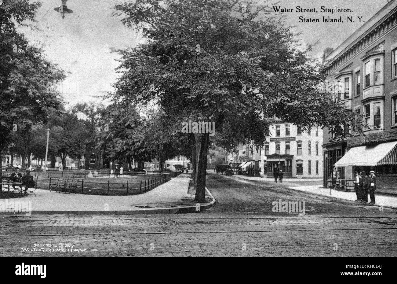Cartolina che mostra la Staten Island Savings Bank all'angolo, negozi, Washington Park di fronte, strada in mattoni con trolley, uomini in piedi sul marciapiede, intitolato 'Water Street, Stapleton, Staten Island, New York', Staten Island, New York, 1900. Dalla Biblioteca pubblica di New York. Foto Stock