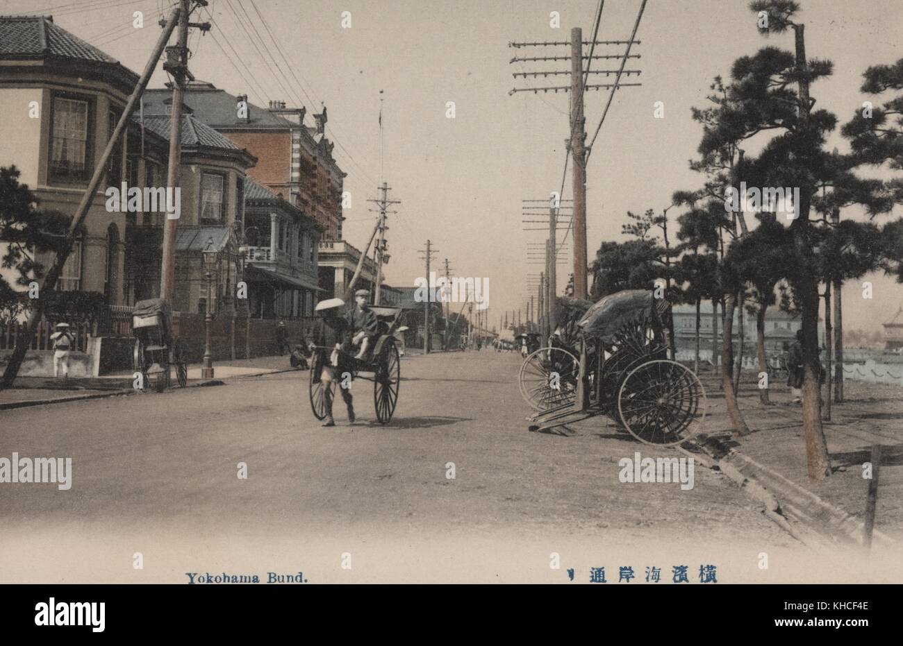 Una foto da cartolina di una vecchia strada giapponese con tre risciò (un vecchio modo di trasporto), con un risciò che viene tirato da un uomo e gli altri due parcheggiati sul lato della strada, Yokohama, Giappone, 1900. Dalla Biblioteca pubblica di New York. Foto Stock