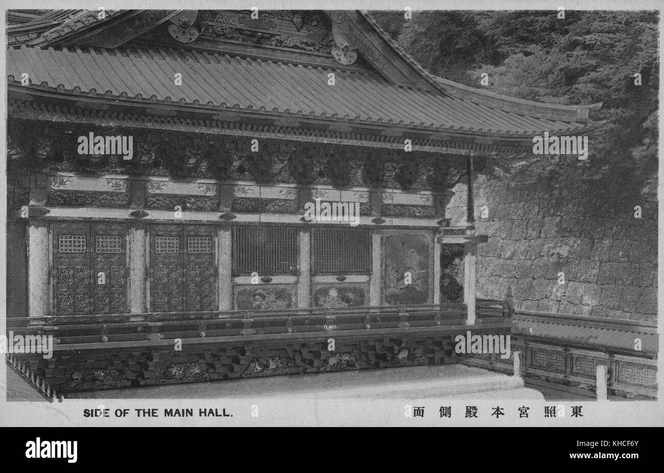 Una cartolina che presenta una vista esterna della sala principale in un Tempio Buddista, l'edificio presenta sculture in legno ed e' protetto da un alto muro di pietra e da alberi, Giappone, 1900. Dalla Biblioteca pubblica di New York. Foto Stock