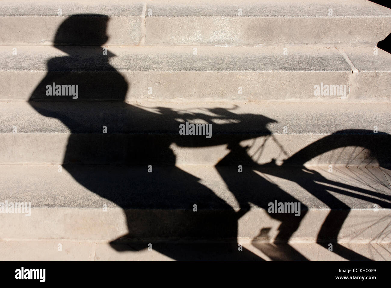 Sfocata ombra di un ciclista con un casco su , spingendo la sua bicicletta fino al pubblico le scale della città Foto Stock