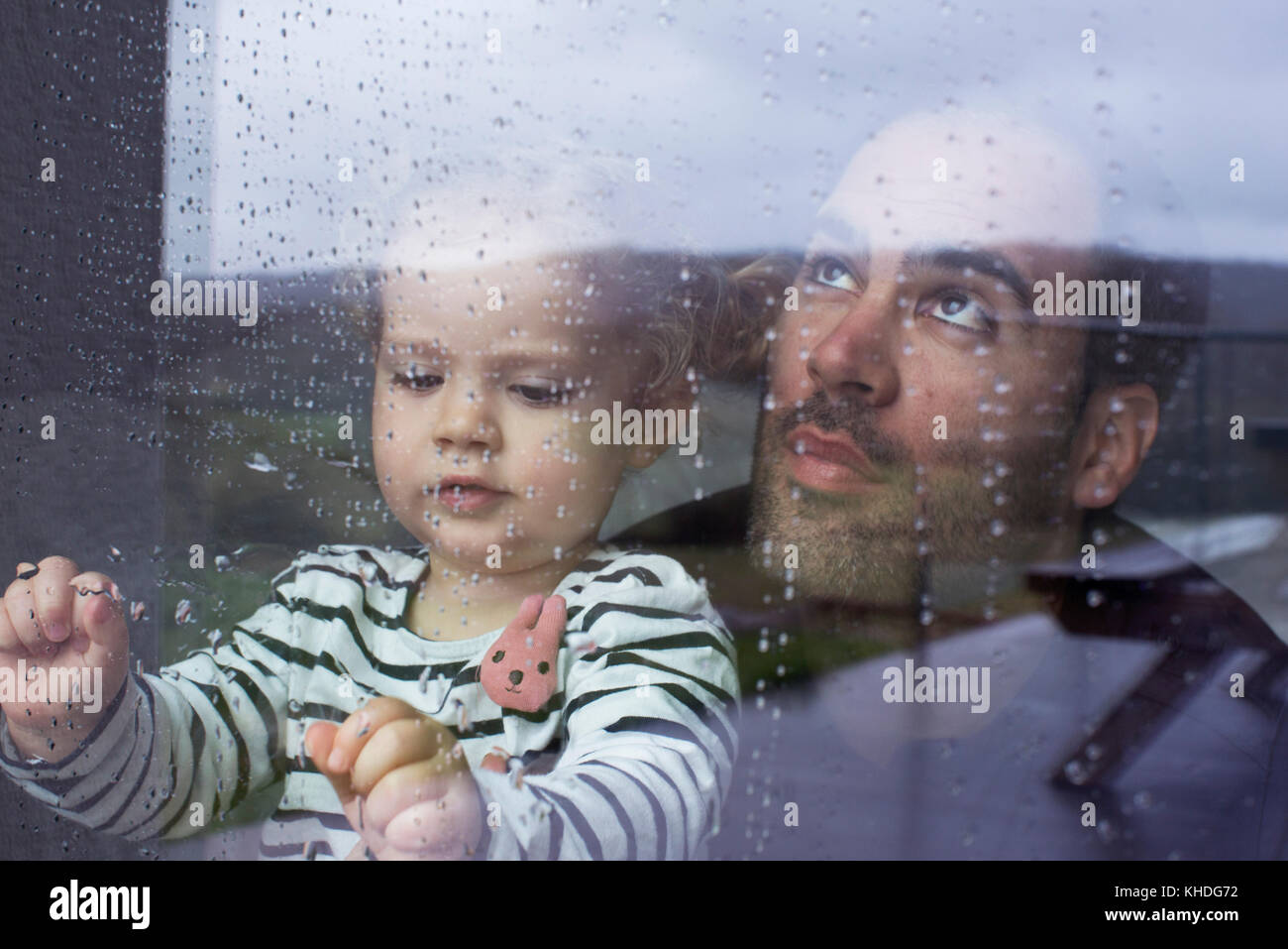 Uomo con bambino guardando attraverso la finestra a guardare la pioggia caduta Foto Stock
