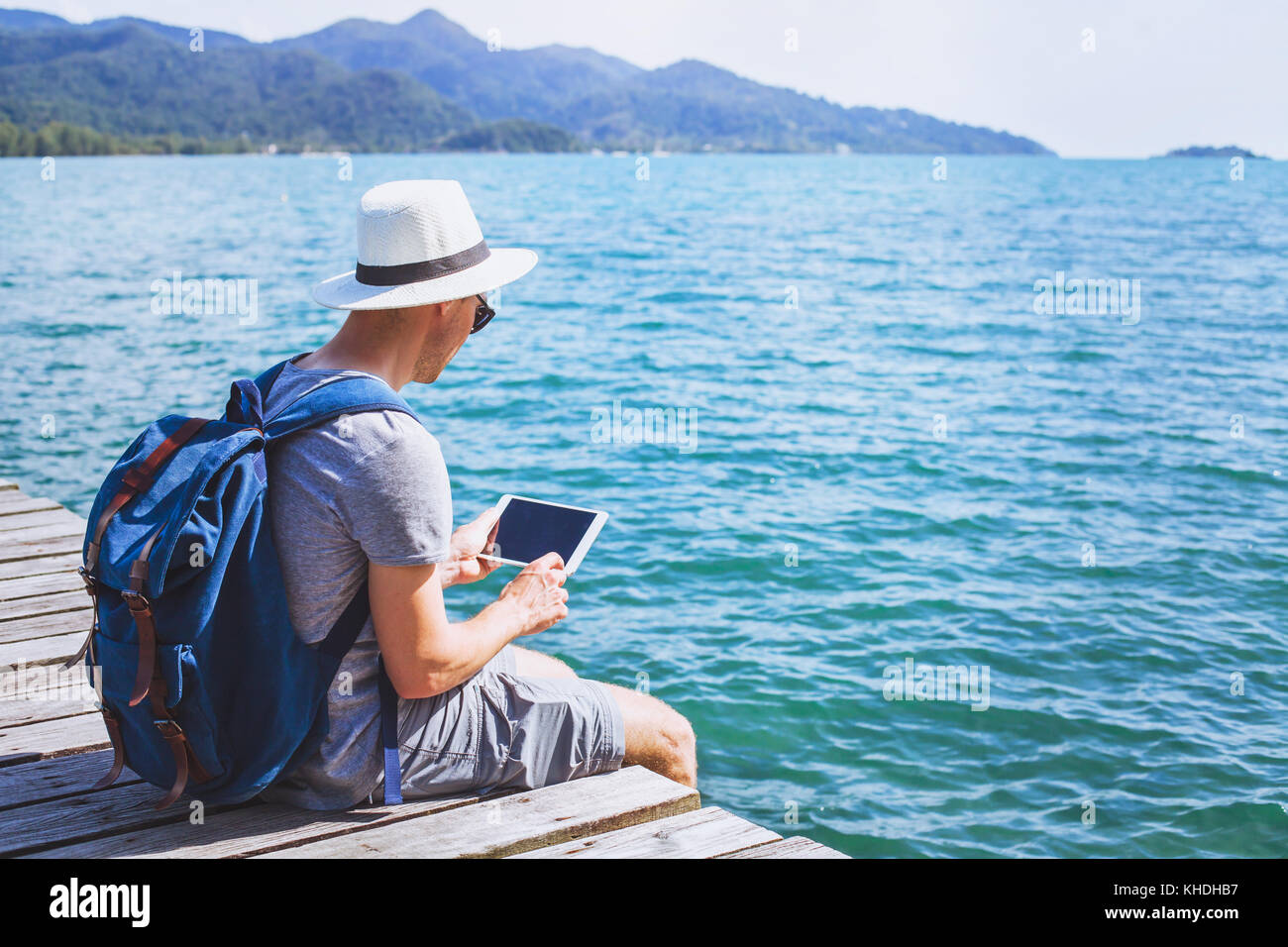 Traveler con tavoletta digitale computer mentre si è seduti sul molo in legno, app di viaggio on-line, uomo backpacker con dispositivo wireless Foto Stock