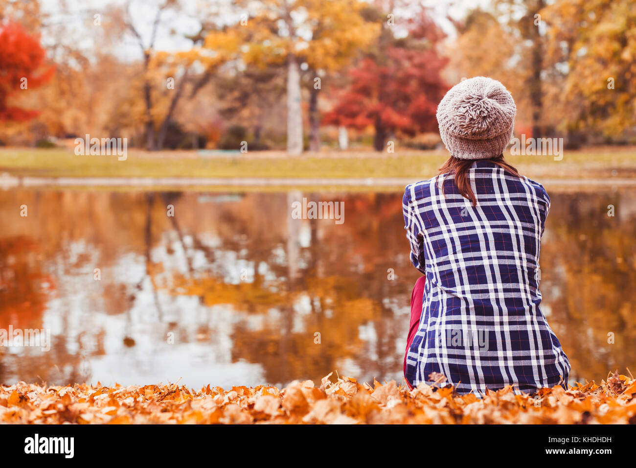 Autunno sfondo accogliente, bella donna seduta vicino al lago nella stagione autunnale Foto Stock