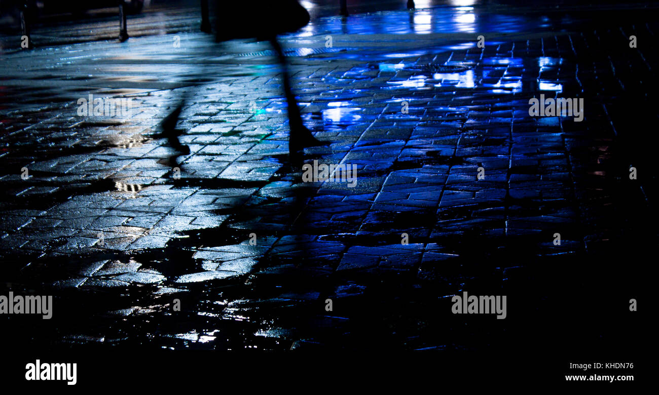Città piovosa street riflessioni: gambe di una giovane donna che cammina nella notte Foto Stock