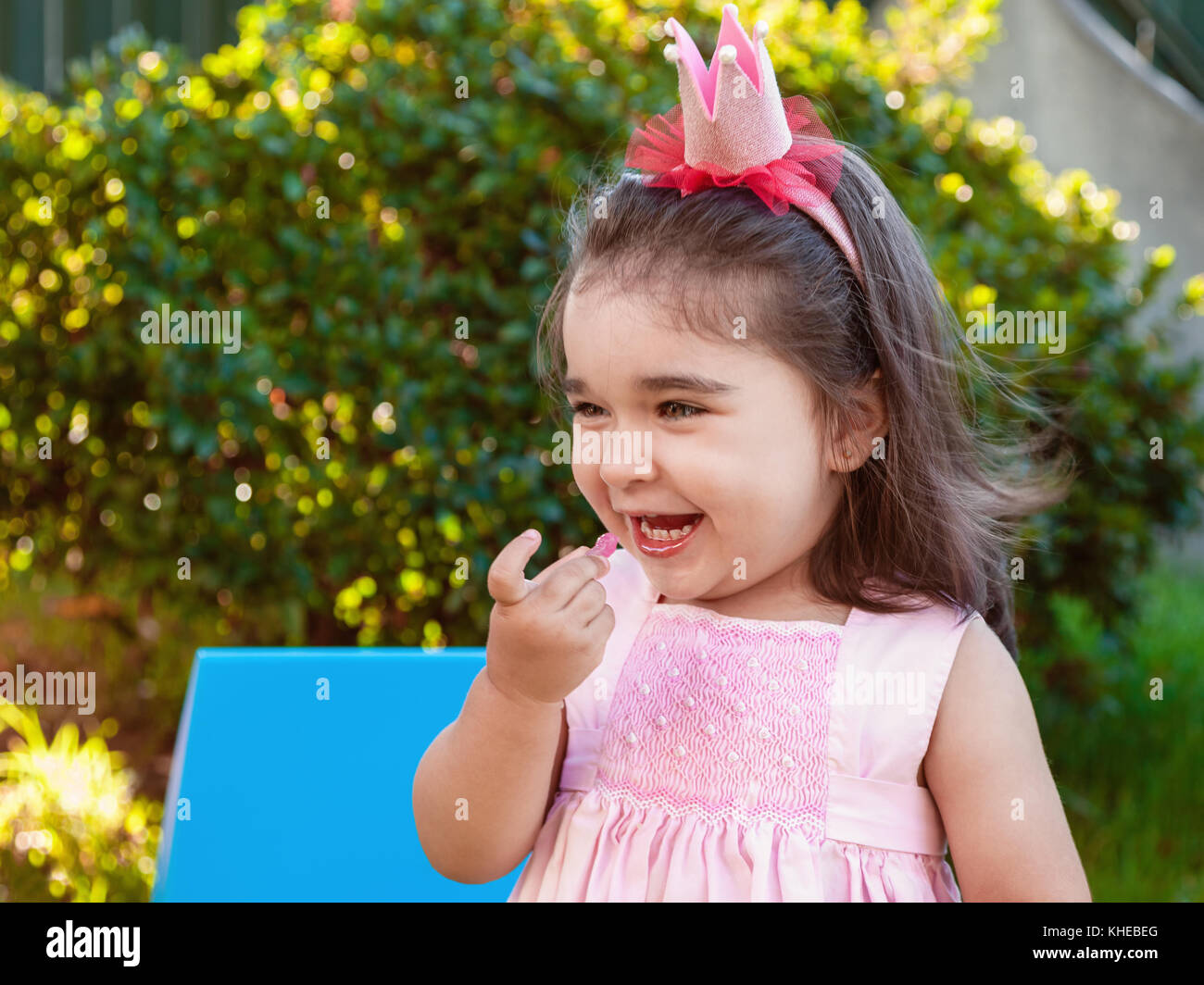 Molto felice baby toddler girl, mangiare gummies ridendo e sorridendo in outdoor partito vestito in abito rosa come principessa o regina con la corona Foto Stock
