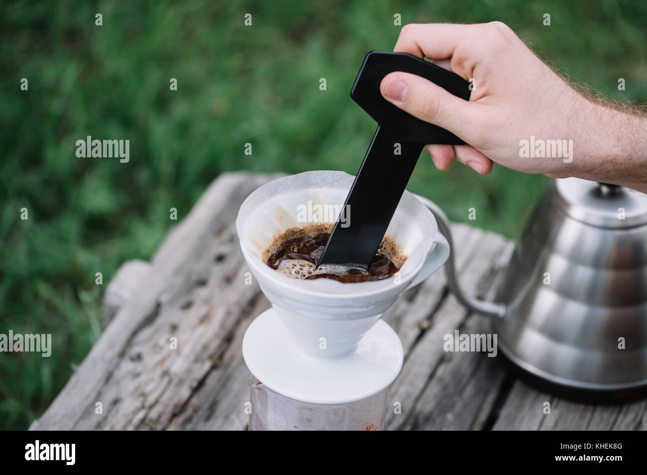 Uomo di caffè di agitazione nel caffè gocciolatore sul tavolo di legno, dehor estivo sullo sfondo Foto Stock