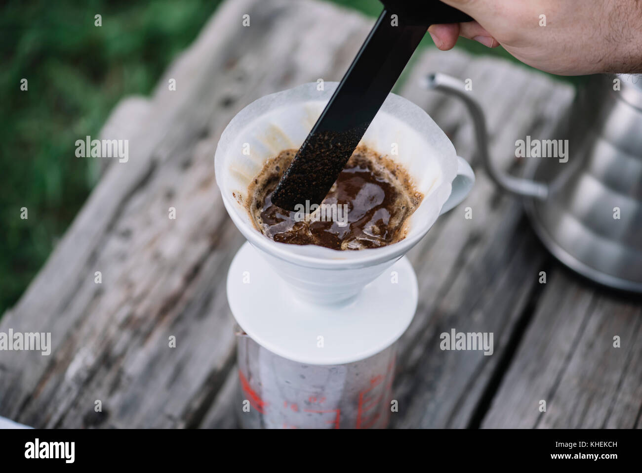 Uomo di caffè di agitazione nel caffè gocciolatore sul tavolo di legno, dehor estivo sullo sfondo Foto Stock