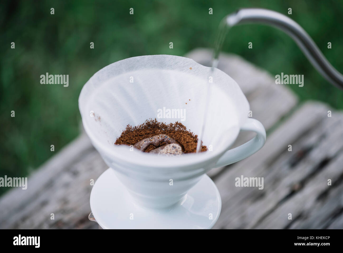 Deliziosi caffè pourover fioritura mentre l'uomo si versa acqua nel gocciolatore a terra i chicchi di caffè. picnic estivo sul vecchio tavolo in legno backgrou Foto Stock